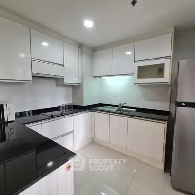 Modern kitchen with sleek white cabinets and black countertops, featuring a built-in microwave and stainless steel fridge.