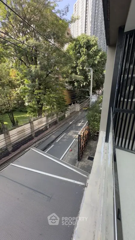 Urban street view from balcony with lush trees and high-rise buildings