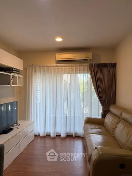 Cozy living room with leather sofa, TV, and large window with curtains.