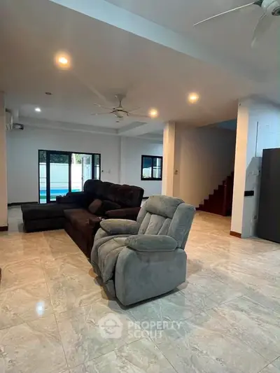 Spacious living room with modern furniture and open layout, featuring a cozy recliner and large windows.