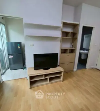 Cozy living room with wooden flooring, TV stand, and open kitchen view in modern apartment.