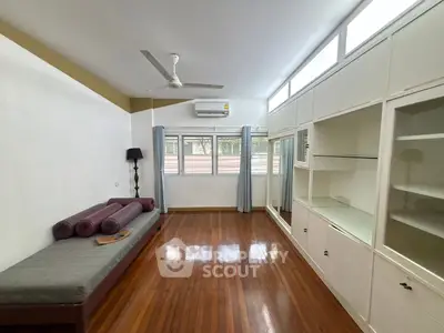 Spacious living room with wooden flooring and built-in storage, featuring large windows and modern ceiling fan.