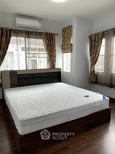 Spacious bedroom with large windows and elegant curtains, featuring a comfortable bed and air conditioning.