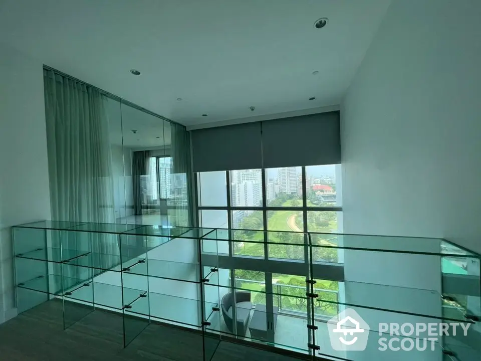 Spacious and modern living room with floor-to-ceiling windows offering a panoramic city view, complemented by a sleek glass balcony railing.