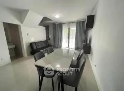 Modern dining area with sleek table and chairs, adjacent to a cozy living space and large window.