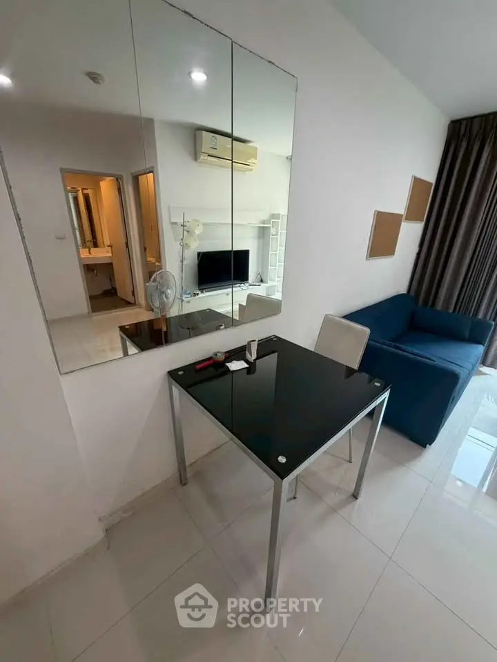 Modern living room with sleek black table, blue sofa, and wall mirror reflecting a TV and air conditioner.