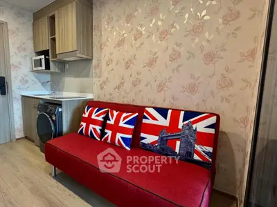 Charming living room with floral wallpaper and modern kitchenette, featuring a vibrant red sofa.