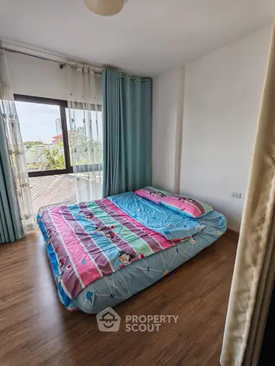 Cozy bedroom with large window and colorful bedding, offering natural light and a serene atmosphere.