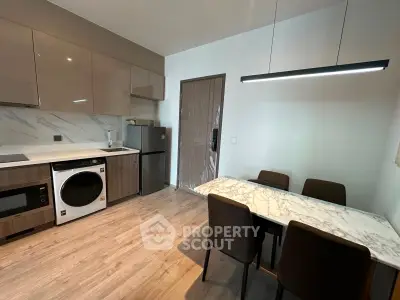 Modern kitchen with sleek appliances and dining area, featuring a washing machine and stylish lighting.