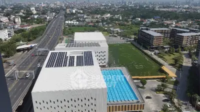 Aerial view of modern building with solar panels, swimming pool, and sports field, ideal for urban living.