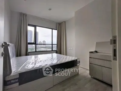 Modern bedroom with large window and city view, featuring a new mattress and sleek dresser.