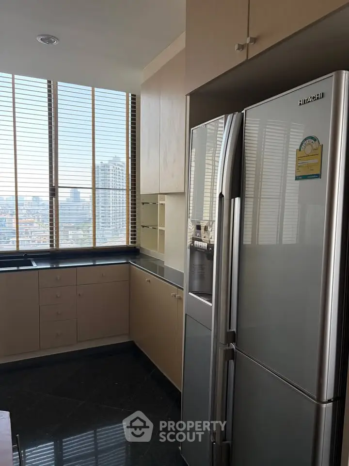 Modern kitchen with sleek refrigerator and city view from large windows.