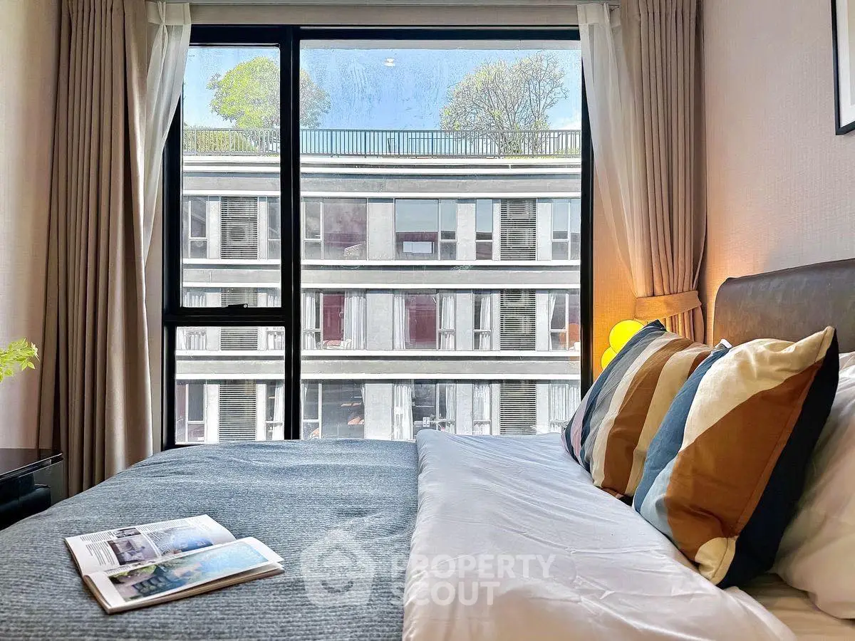 Modern bedroom with large window offering a stunning view of a contemporary building.