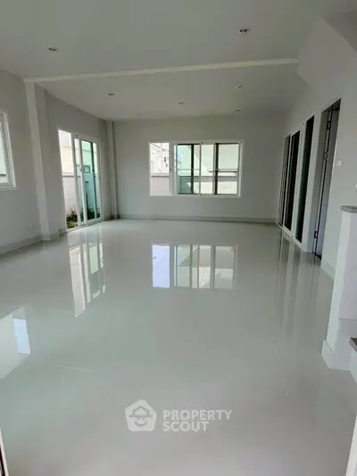 Spacious empty living room with large windows and glossy tiled floor in modern home.