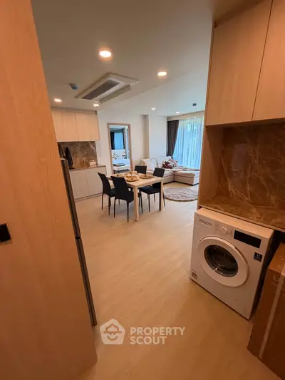 Modern open-plan living room with dining area and washing machine in stylish apartment.