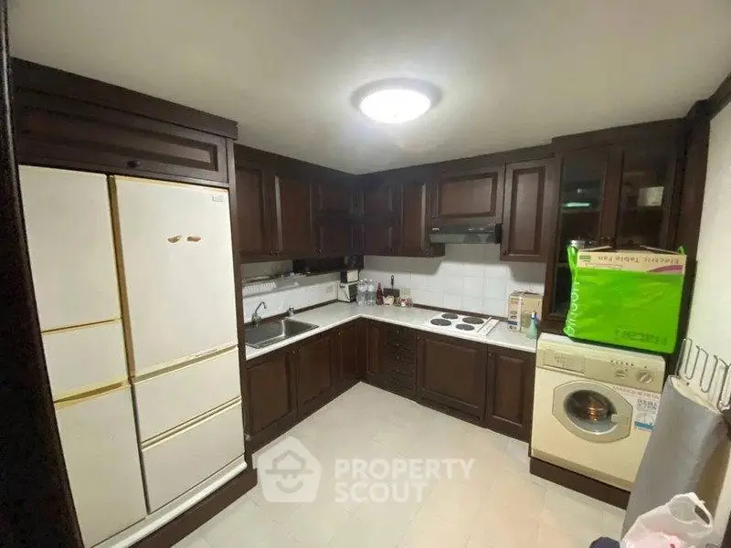 Spacious kitchen with dark wood cabinets, washing machine, and ample storage space.