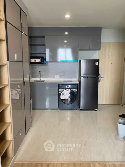 Modern kitchen with sleek cabinets, washing machine, and stainless steel fridge in compact apartment.