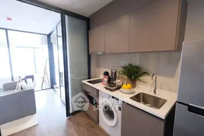 Modern kitchen with sleek cabinetry, washing machine, and open layout leading to a bright living area.