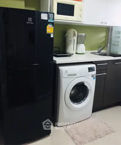 Modern kitchen with sleek appliances including fridge, washing machine, and microwave in compact layout.