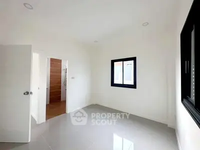Spacious empty room with modern white walls and large window, perfect for customization.