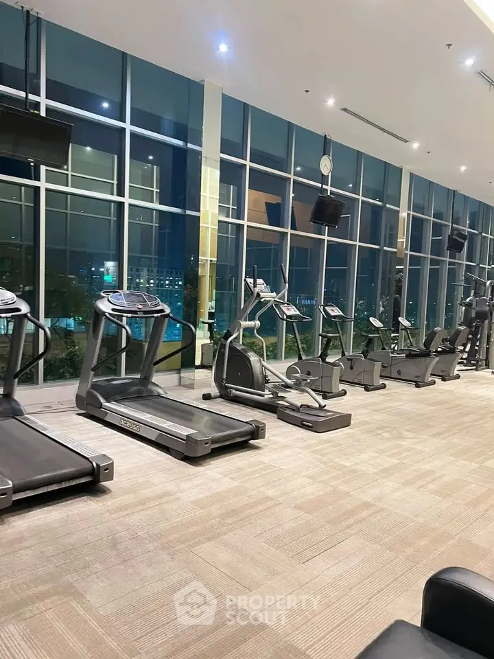 Spacious modern gym with large windows and state-of-the-art equipment in luxury building.
