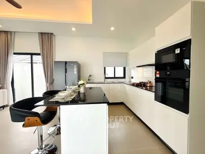 Modern kitchen with sleek white cabinets and black countertops, featuring built-in appliances and stylish bar seating.
