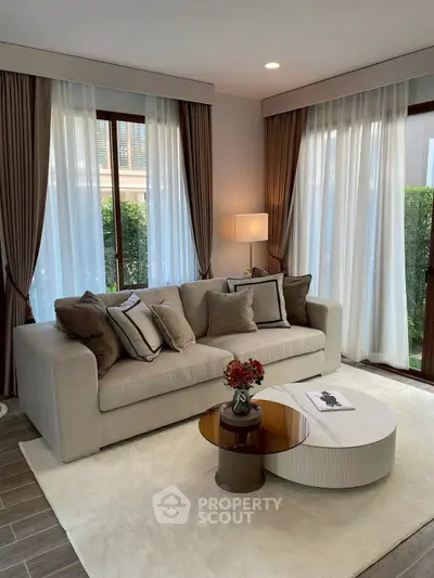 Elegant living room with modern sofa, stylish coffee table, and large windows with lush garden view.