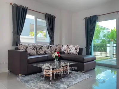 Elegant living room with modern sofa and glass coffee table, featuring large windows and lush garden view.