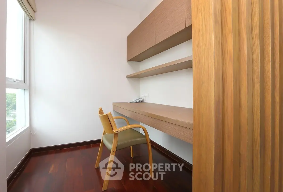 Modern study room with wooden flooring and built-in shelves, featuring a large window for natural light.