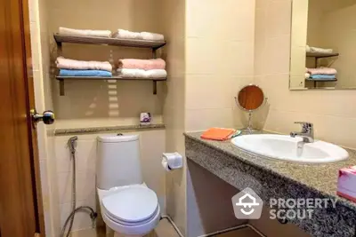 Compact modern bathroom with granite countertop sink, well-organized shelves with fresh towels, and a clean, white toilet.