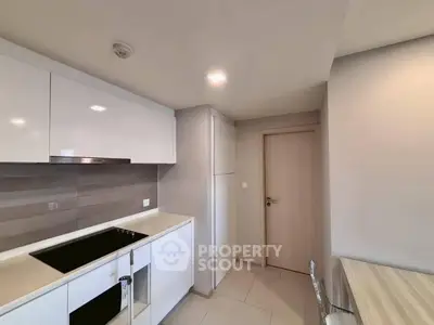 Modern kitchen with sleek white cabinetry and electric cooktop in a contemporary apartment.