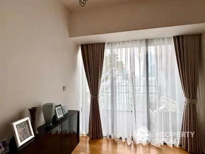 Bright room with floor-to-ceiling windows and elegant curtains leading to a balcony.