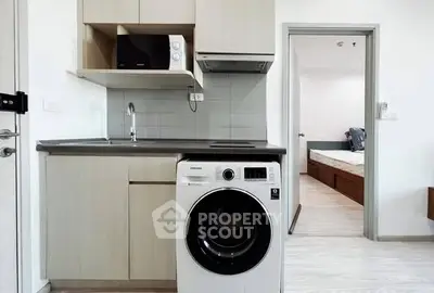 Modern compact kitchen with washing machine and microwave, adjacent to a cozy bedroom.