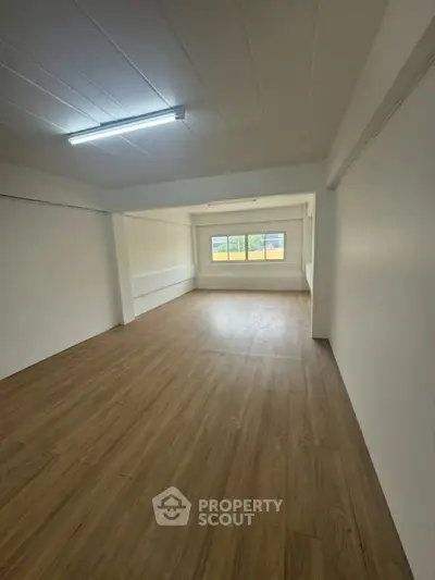 Spacious empty room with wooden flooring and large window, ideal for customization.