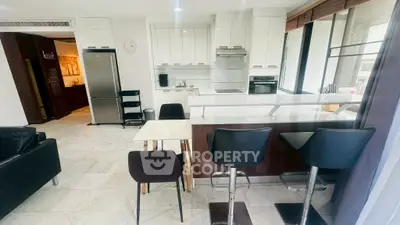 Modern kitchen with sleek white cabinets, breakfast bar, and stainless steel appliances in open layout.