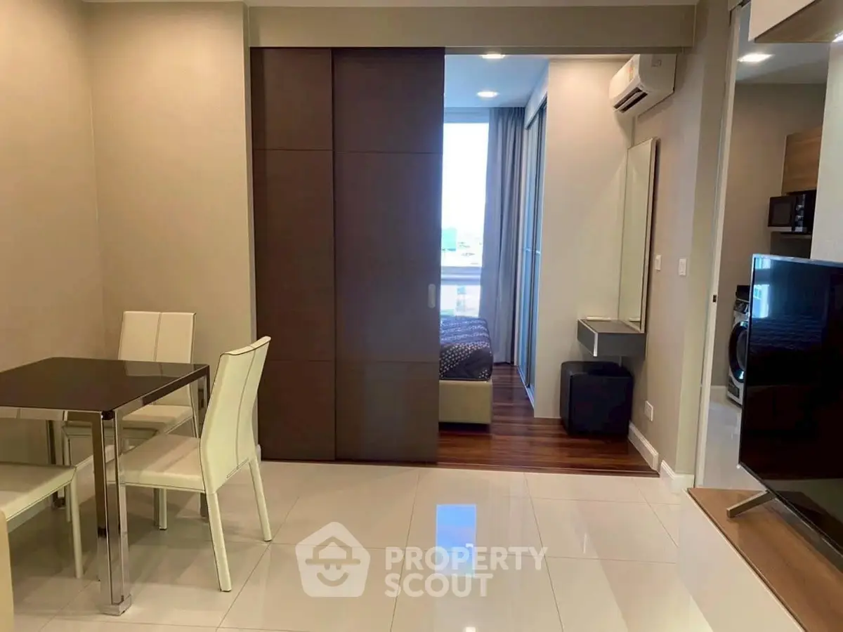 Modern apartment interior with dining area and bedroom, featuring sleek furniture and contemporary design.