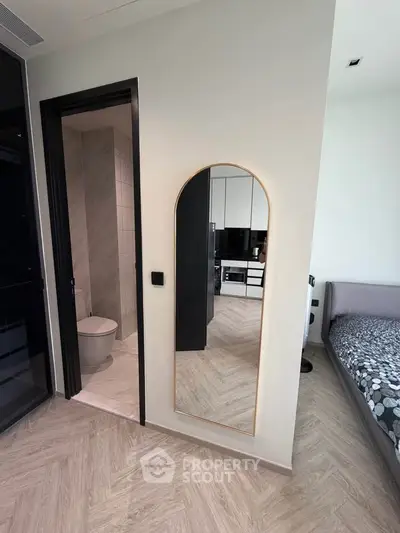 Modern apartment interior with sleek bathroom and cozy bedroom, featuring stylish mirror and herringbone flooring.
