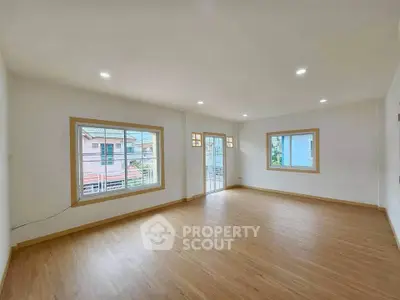Spacious empty living room with large windows and wooden flooring.
