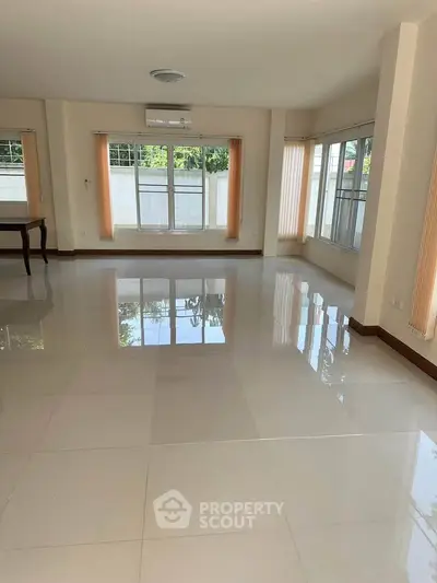 Spacious empty living room with large windows and glossy tiled floors, perfect for natural light and modern living.