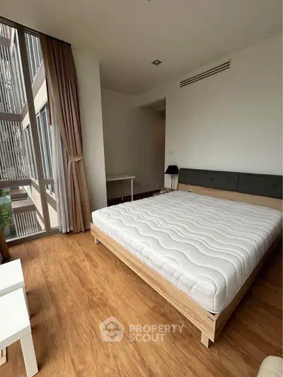 Spacious bedroom with large window and modern furnishings in a stylish apartment.