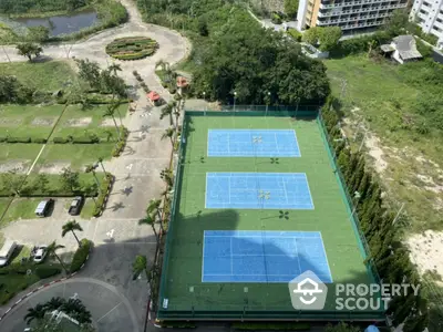 Aerial view of tennis courts in a residential complex with lush greenery and parking area.