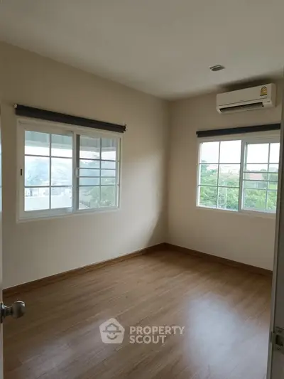 Bright empty bedroom with wooden flooring and large windows
