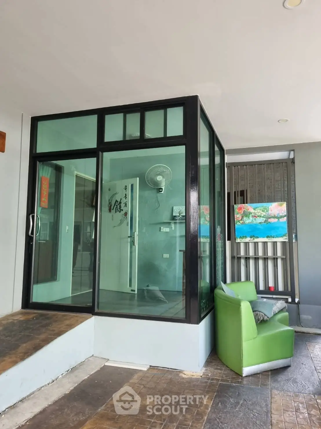Modern glass entrance with green armchair and decorative art, ideal for stylish office or home
