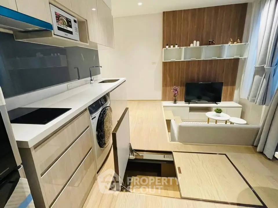 Modern open-plan living room with sleek kitchen and hidden storage, featuring a washing machine and stylish decor.