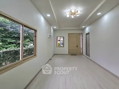 Spacious and bright living room with modern lighting and large windows offering lush green views.