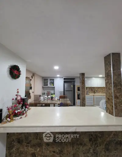 Modern kitchen with marble accents and festive decor, featuring open layout and stainless steel appliances.