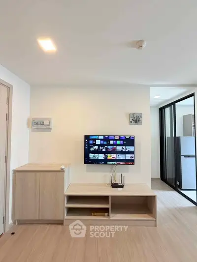 Modern living room with wall-mounted TV and sleek wooden furniture in a bright apartment.