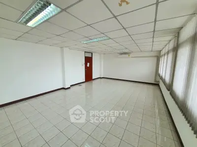 Spacious empty room with tiled flooring and large windows, ideal for office or studio space.