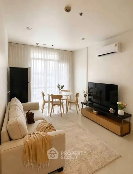 Modern living room with cozy beige sofa, large TV, and dining area in a bright apartment.