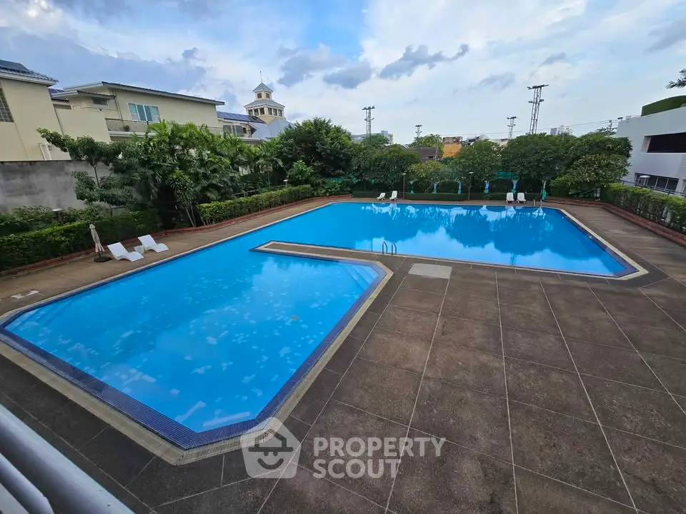 Spacious outdoor pool area with lush greenery and clear blue sky.
